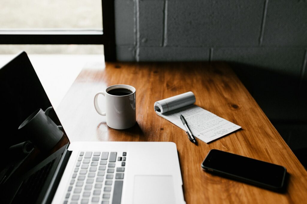 Person working on a laptop at a wooden desk with notebook and coffee, blogging setup for SEO content writing