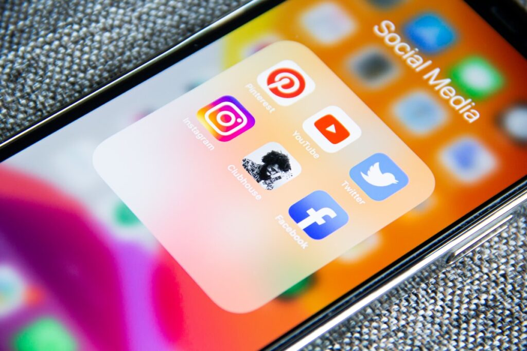 Social media icons displayed on a smartphone next to a notebook and pen on a desk