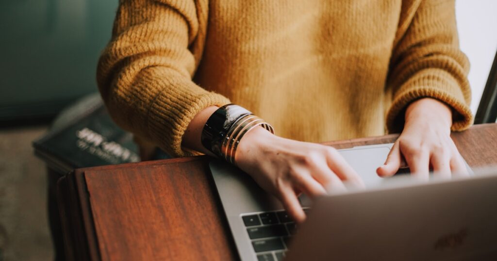 Blogger writing a product review on a laptop with notebooks and coffee on a wooden desk